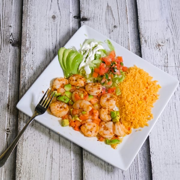 Shrimp with avocado, pico de gallo, lettuce, sour cream, and orange rice on a white plate.